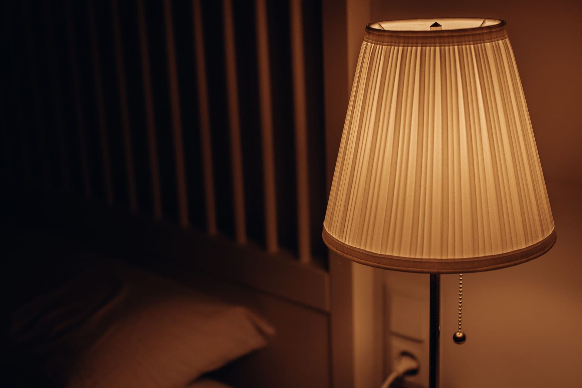 A dark bedroom with soft light from a bedside lamp
