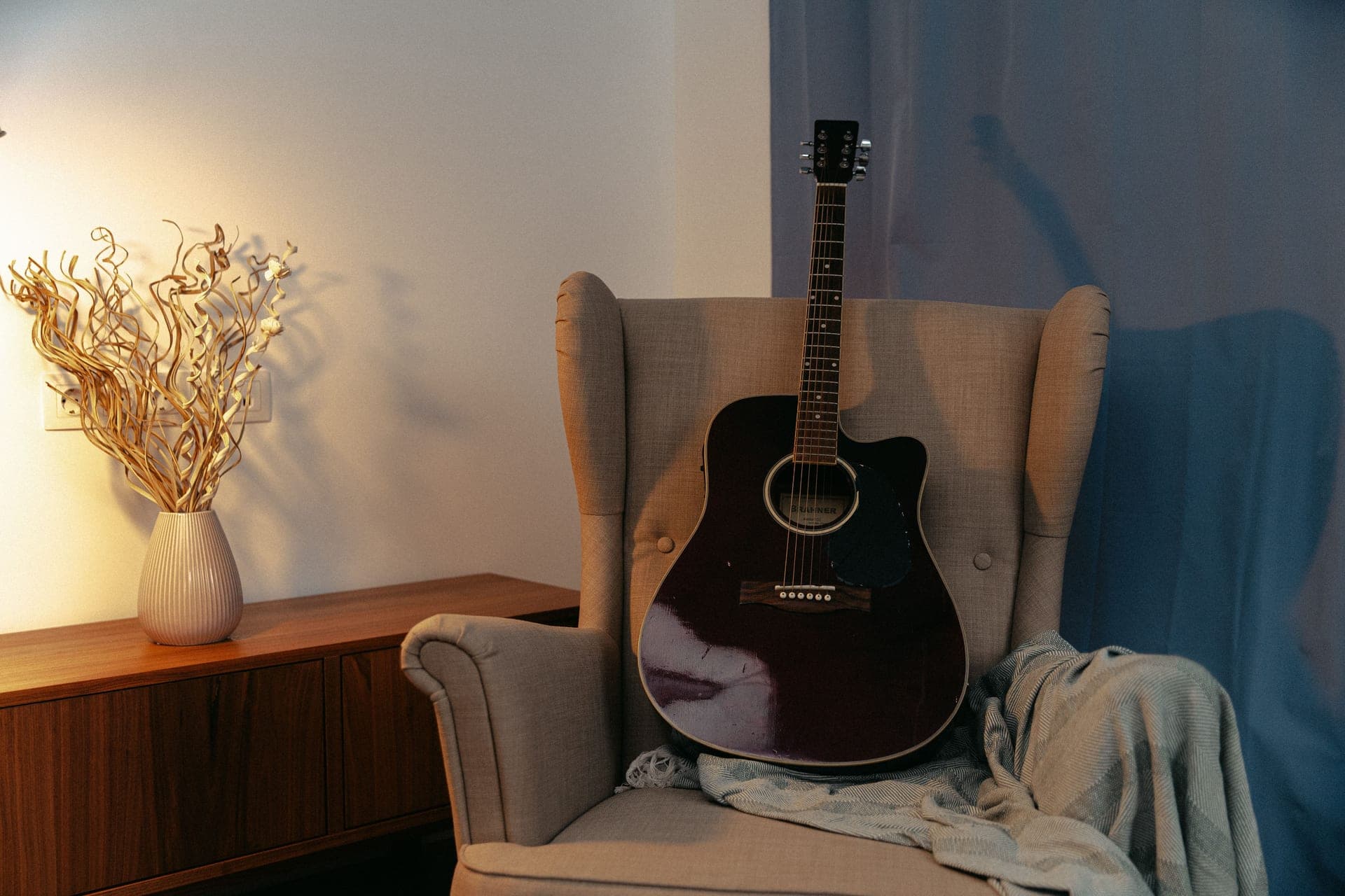 An acoustic guitar resting on an armchair in a warmly lit room