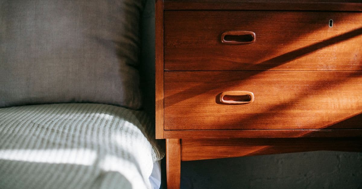 A made bed beside a wooden nightstand in morning light
