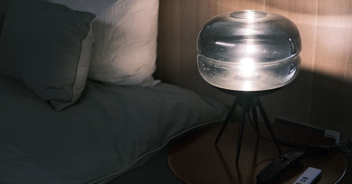 A dark bedroom lit only by a small bedside lamp