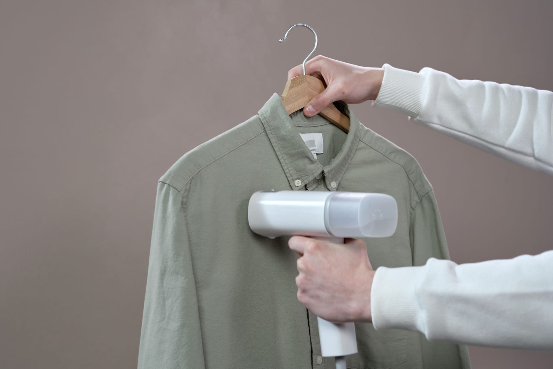 A handheld garment steamer being used on fabric